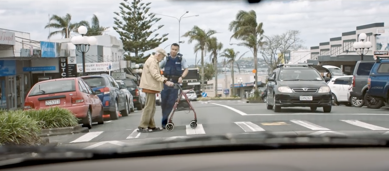 Image of male police officer helping an elderly man with his walker cross the street safely