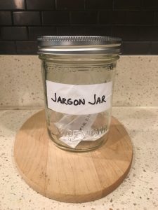 Image of the Jargon Jar with pieces of paper inside that contain jargon phrases, and will include circle back after this post is done