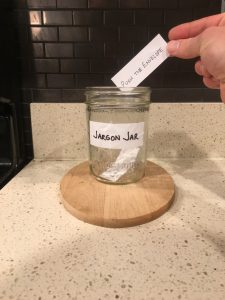 Image of a hand placing a handwritten 'Push the envelope' note into the Jargon Jar