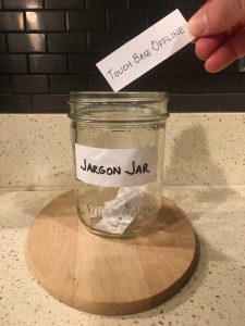 Image of a hand placing a handwritten Touch base offline note into the Jargon Jar